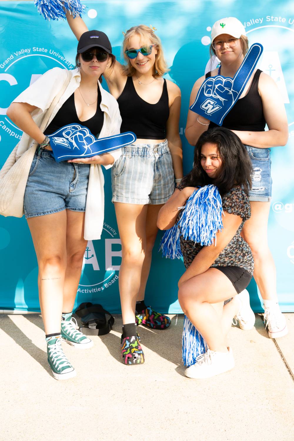 four students posing in front of CAB backdrop at Laker Kickoff photo booth with pom poms and foam fingers
